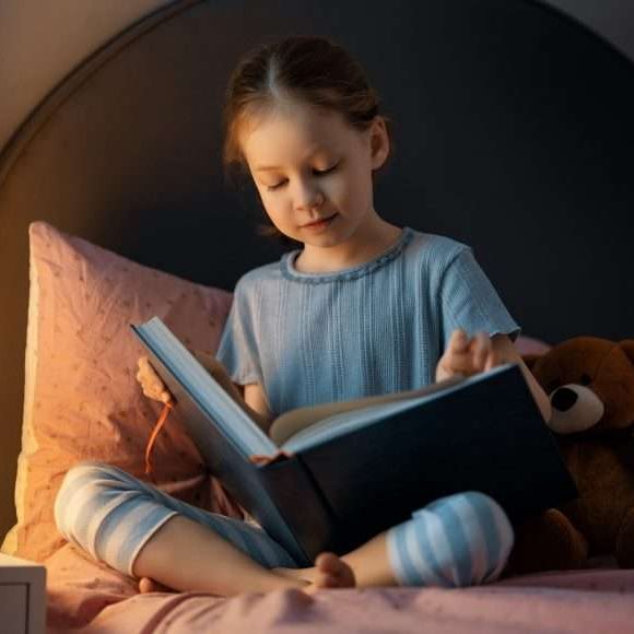 Cute little girl is reading a book in her bedroom.