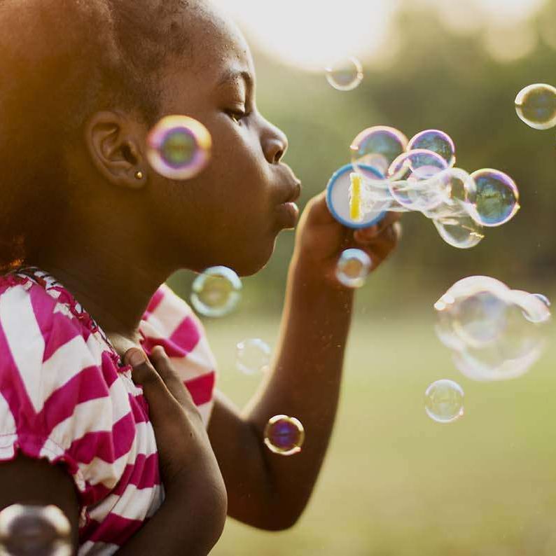 African descent girl playing blowing bubble in a park