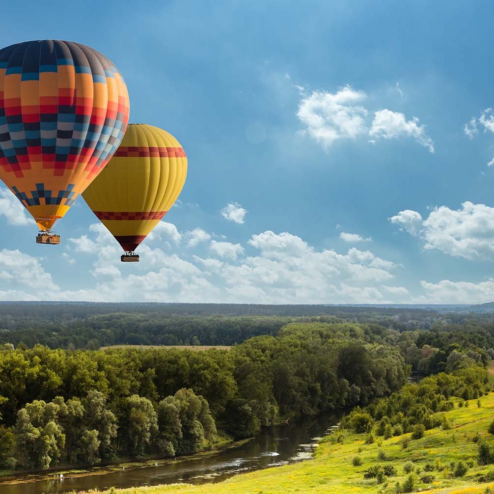 Colorful hot air balloon flying over green field and river